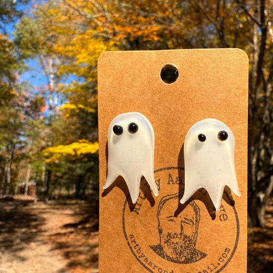 Hand blown glass ghost stud earrings on a kraft card in front of fall trees