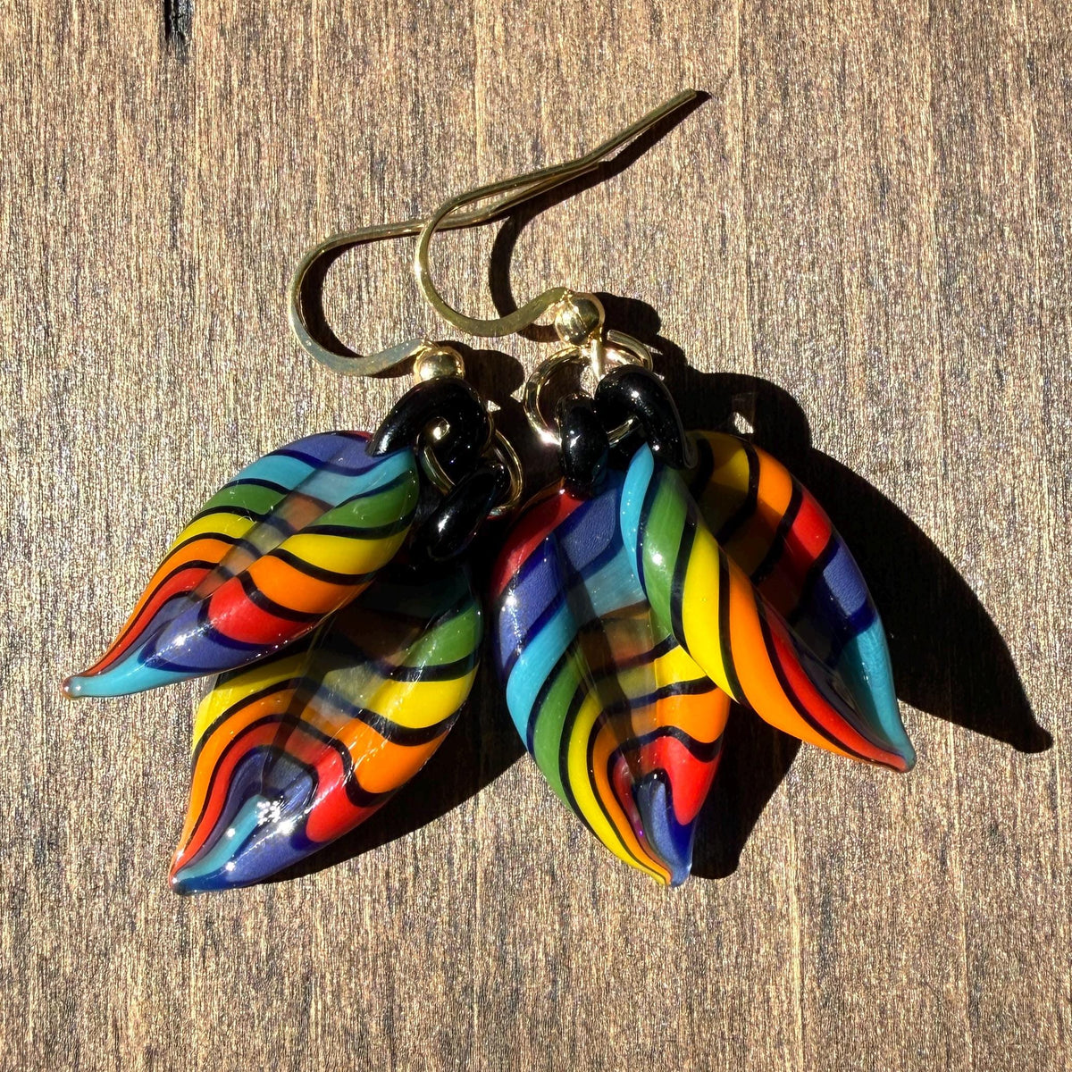 Pair of rainbow glass leaf dangle earrings with black accents laid flat